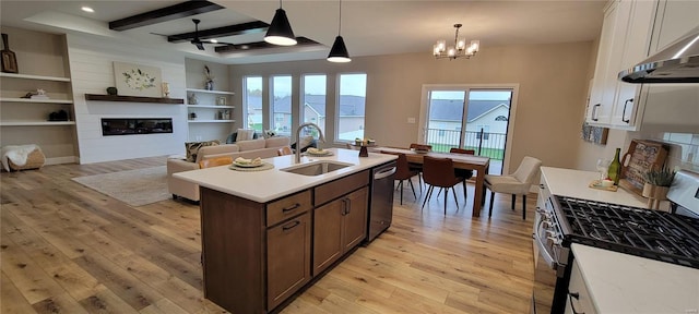 kitchen with sink, stainless steel appliances, range hood, decorative light fixtures, and a fireplace