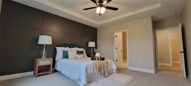 bedroom with a tray ceiling, ceiling fan, ensuite bathroom, and light carpet