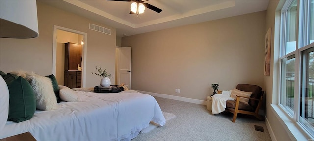 carpeted bedroom with a raised ceiling, connected bathroom, and ceiling fan