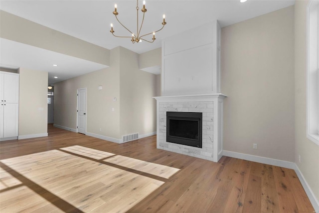 unfurnished living room featuring light hardwood / wood-style floors, a notable chandelier, and a brick fireplace