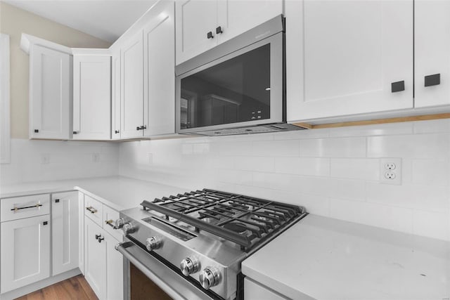 kitchen featuring decorative backsplash, appliances with stainless steel finishes, light wood-type flooring, and white cabinetry