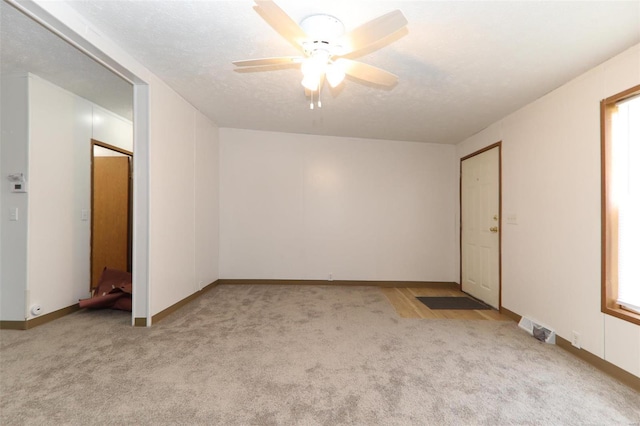 empty room featuring light carpet, ceiling fan, and a textured ceiling