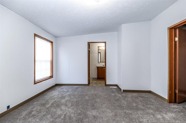 unfurnished bedroom with carpet flooring, ensuite bath, and a textured ceiling