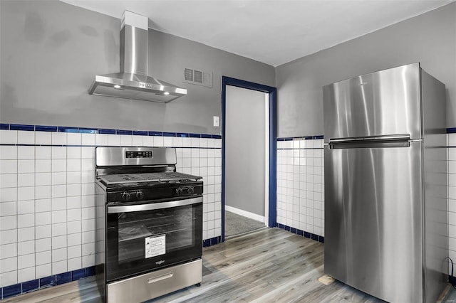 kitchen featuring light wood-type flooring, wall chimney range hood, stainless steel appliances, and tile walls