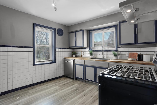 kitchen featuring wood counters, stainless steel dishwasher, tile walls, and sink