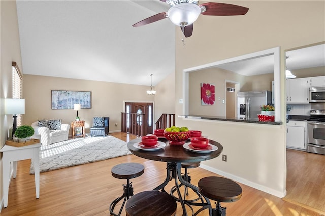 dining space featuring ceiling fan with notable chandelier, high vaulted ceiling, and light wood-type flooring