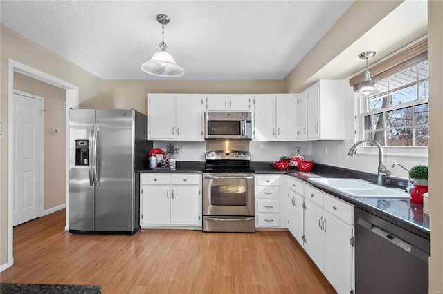 kitchen with white cabinets, decorative light fixtures, stainless steel appliances, light hardwood / wood-style floors, and sink