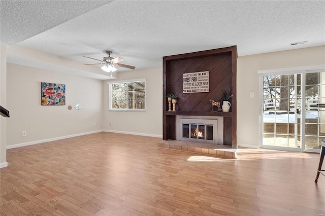 unfurnished living room featuring ceiling fan, light hardwood / wood-style floors, a textured ceiling, and a fireplace