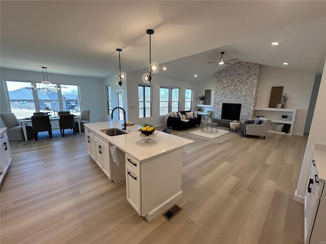 kitchen with a stone fireplace, dishwasher, light wood-type flooring, and a sink