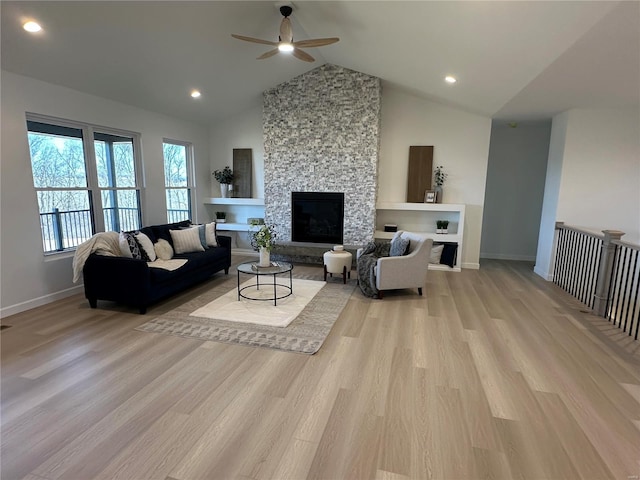 living area featuring light wood-type flooring, baseboards, high vaulted ceiling, and a stone fireplace