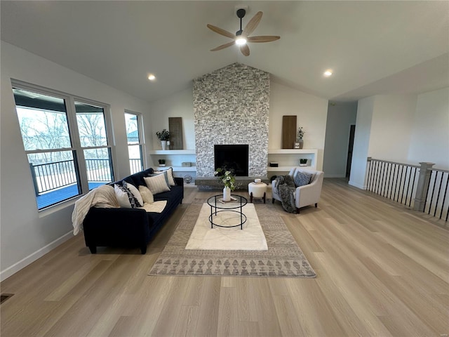 living room featuring baseboards, light wood-style flooring, recessed lighting, a stone fireplace, and vaulted ceiling