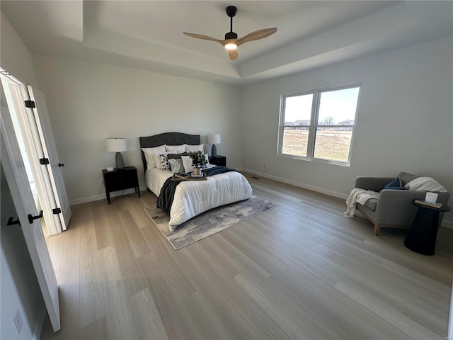 bedroom featuring a tray ceiling, baseboards, light wood-style flooring, and a ceiling fan