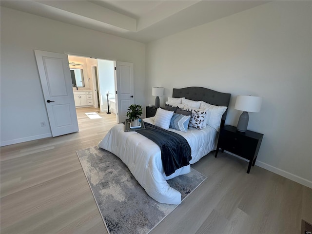 bedroom featuring baseboards, light wood finished floors, and connected bathroom