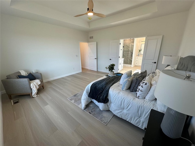 bedroom with a tray ceiling, light wood-style flooring, visible vents, and baseboards