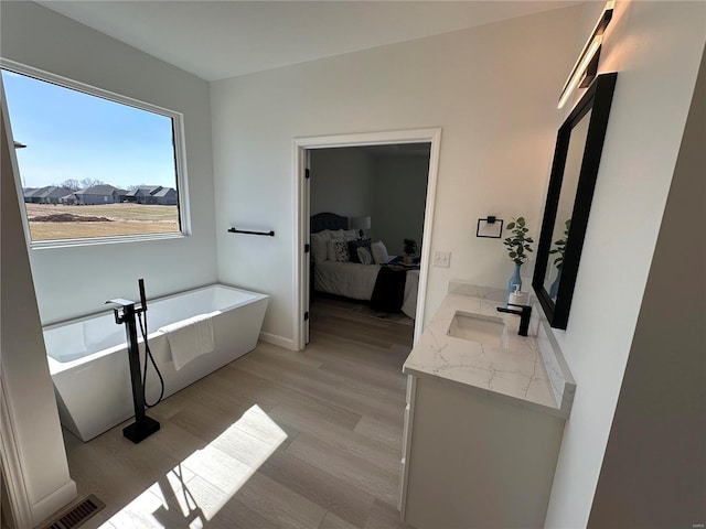 full bathroom with visible vents, wood finished floors, connected bathroom, a soaking tub, and vanity