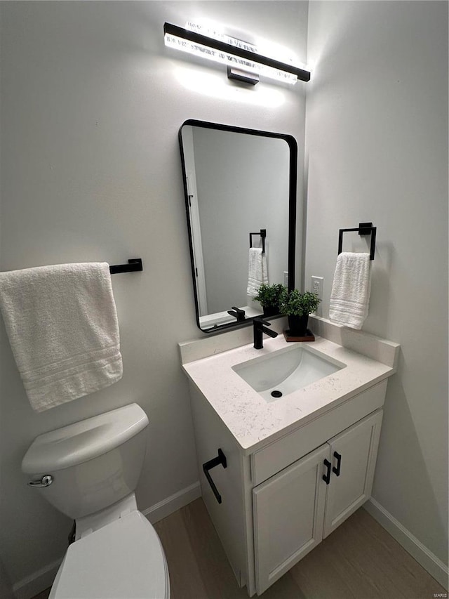 half bath with baseboards, toilet, wood finished floors, and vanity