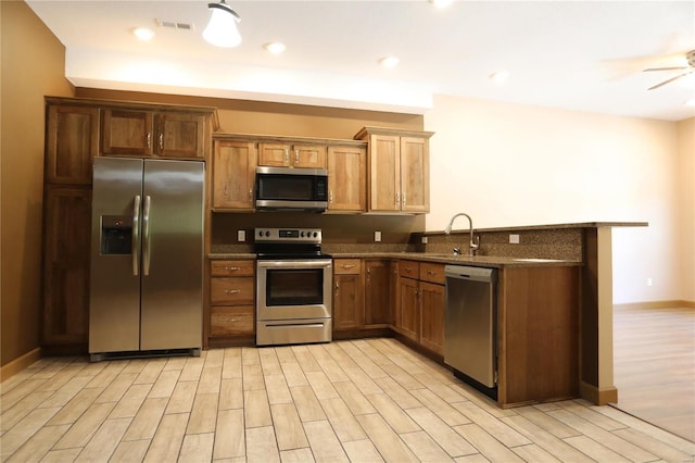 kitchen with light wood-type flooring, kitchen peninsula, stainless steel appliances, sink, and ceiling fan