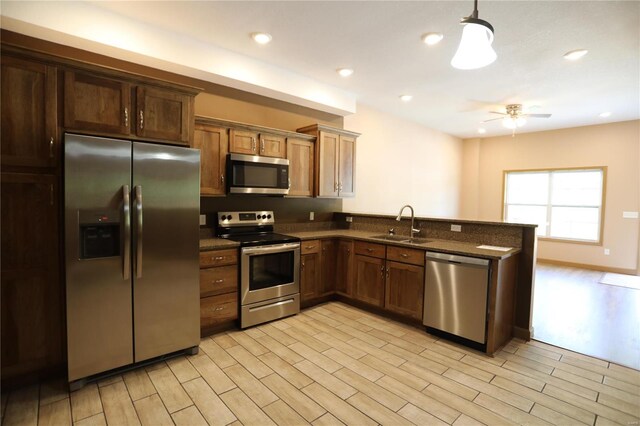 kitchen featuring appliances with stainless steel finishes, hanging light fixtures, ceiling fan, light hardwood / wood-style floors, and sink