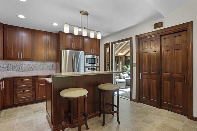 kitchen with a center island, stainless steel appliances, a kitchen breakfast bar, backsplash, and decorative light fixtures