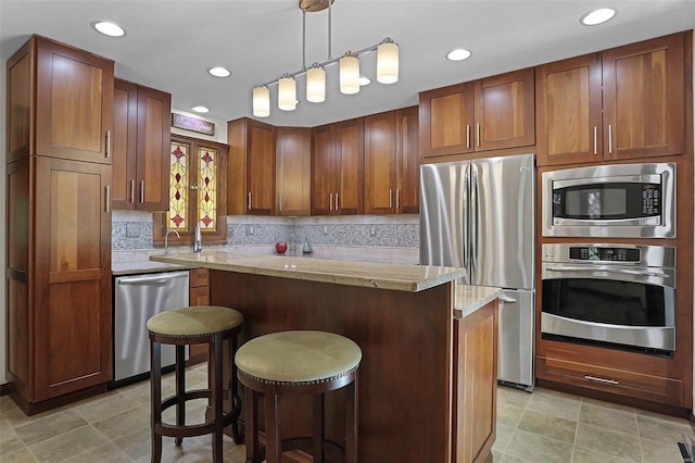 kitchen featuring light stone countertops, appliances with stainless steel finishes, a breakfast bar, a center island, and hanging light fixtures