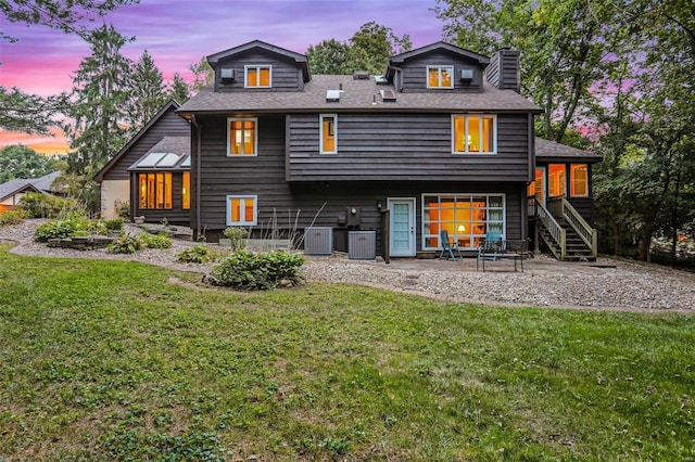 back house at dusk featuring a lawn and central AC