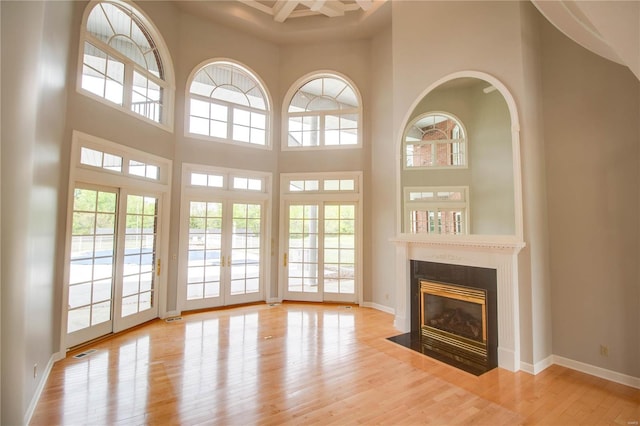 unfurnished living room with a healthy amount of sunlight, a towering ceiling, light wood-type flooring, and a high end fireplace