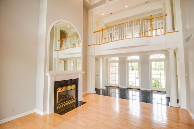 living room with a tiled fireplace, a towering ceiling, hardwood / wood-style flooring, and ornate columns