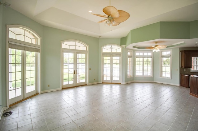 unfurnished living room with a tray ceiling, french doors, plenty of natural light, and tile floors