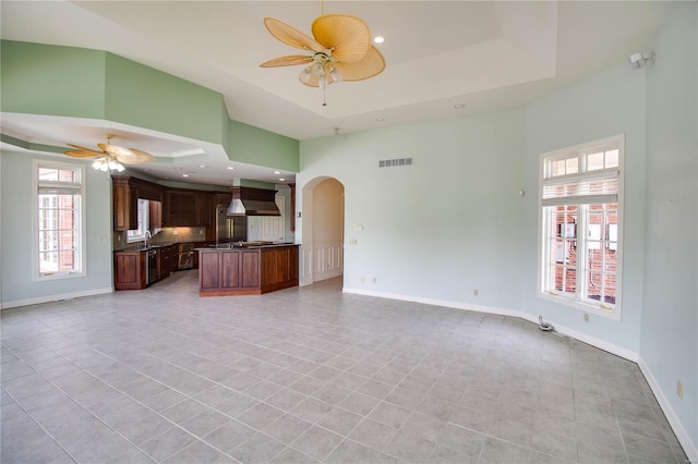 unfurnished living room with ceiling fan, a tray ceiling, and light tile floors