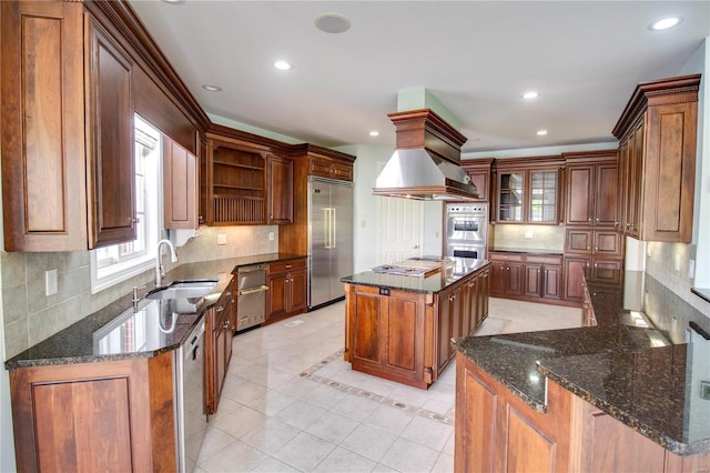 kitchen featuring a kitchen island, appliances with stainless steel finishes, premium range hood, dark stone counters, and light tile floors