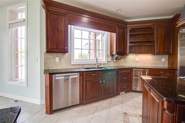 kitchen featuring dark stone counters, tasteful backsplash, dishwasher, light tile floors, and sink