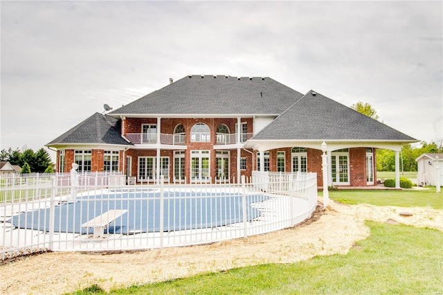 rear view of property featuring a covered pool, a lawn, a balcony, and a patio area