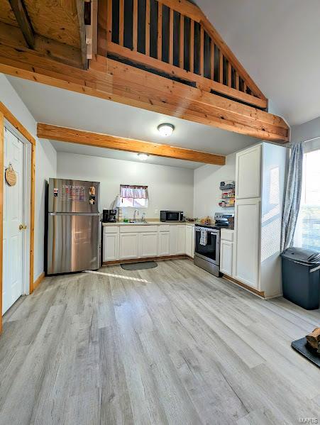 kitchen with appliances with stainless steel finishes, light hardwood / wood-style flooring, lofted ceiling with beams, white cabinetry, and sink