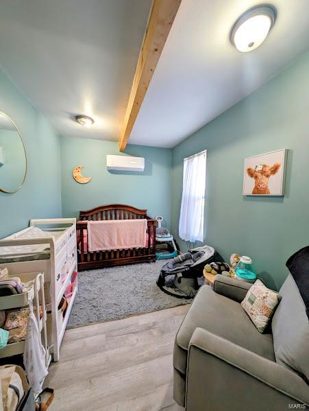 bedroom featuring a wall mounted AC, beam ceiling, and hardwood / wood-style flooring