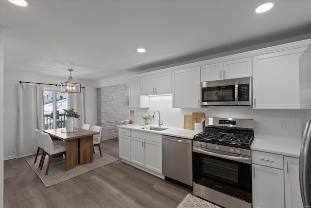 kitchen with sink, light hardwood / wood-style flooring, hanging light fixtures, stainless steel appliances, and white cabinets