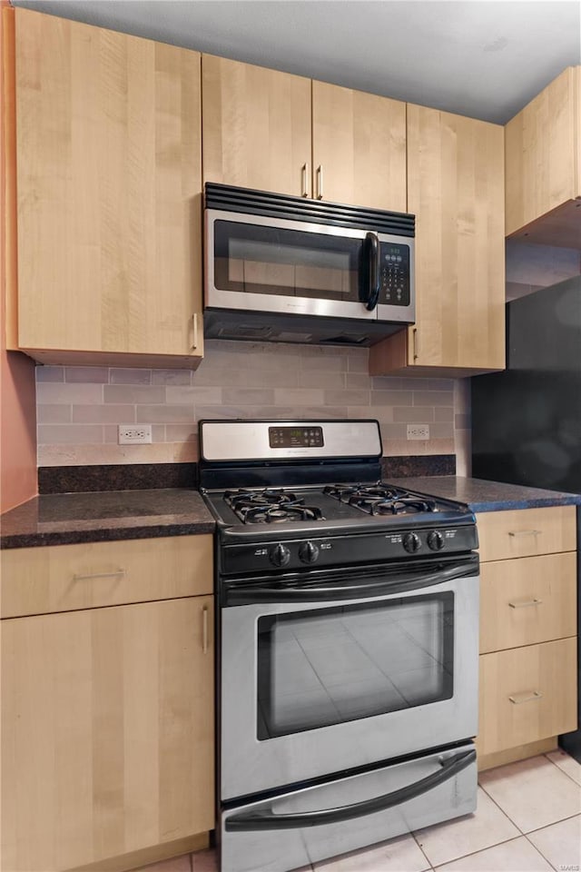 kitchen featuring light brown cabinetry, light tile patterned floors, appliances with stainless steel finishes, and dark stone countertops