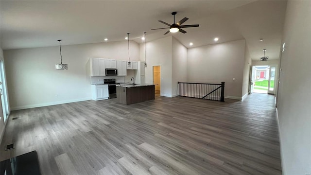 interior space with a center island with sink, appliances with stainless steel finishes, white cabinetry, light wood-type flooring, and decorative light fixtures