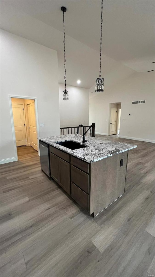 kitchen featuring hardwood / wood-style floors, hanging light fixtures, light stone countertops, stainless steel dishwasher, and sink