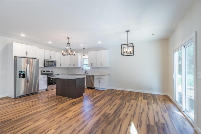 kitchen with decorative light fixtures, a kitchen island, stainless steel appliances, and a wealth of natural light