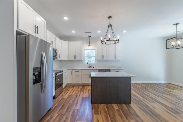 kitchen featuring white cabinets, decorative light fixtures, appliances with stainless steel finishes, dark hardwood / wood-style floors, and a center island