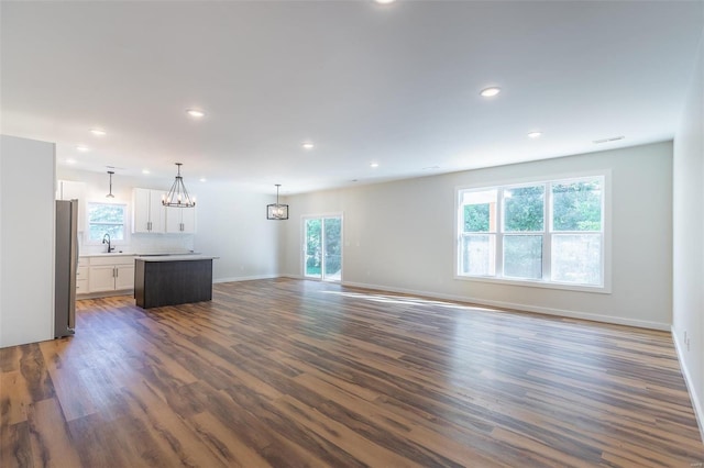 unfurnished living room featuring an inviting chandelier, sink, a healthy amount of sunlight, and dark hardwood / wood-style flooring