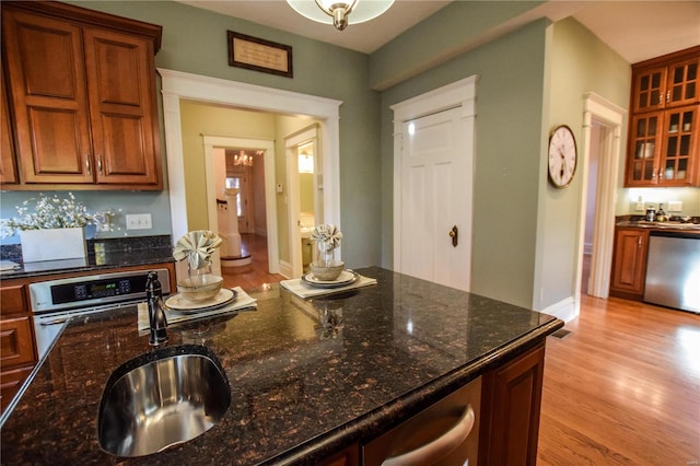 kitchen featuring appliances with stainless steel finishes, dark stone counters, sink, a chandelier, and light hardwood / wood-style floors