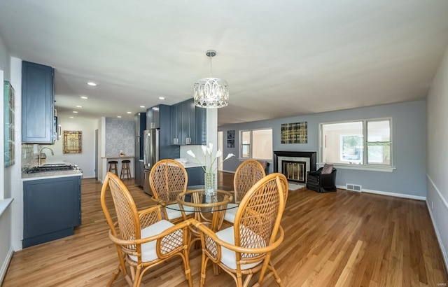 dining room with sink, a high end fireplace, a chandelier, and light wood-type flooring