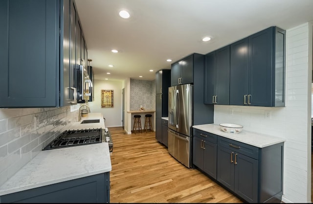 kitchen featuring appliances with stainless steel finishes, light wood-type flooring, tasteful backsplash, and blue cabinets