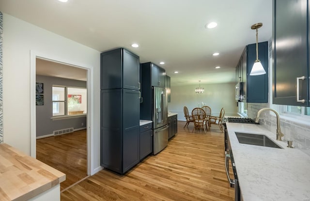 kitchen with sink, hanging light fixtures, tasteful backsplash, light hardwood / wood-style flooring, and stainless steel fridge