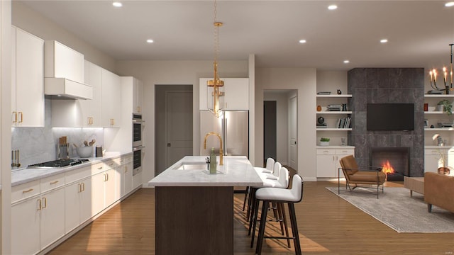 kitchen with white cabinets, a tiled fireplace, decorative light fixtures, a center island with sink, and sink