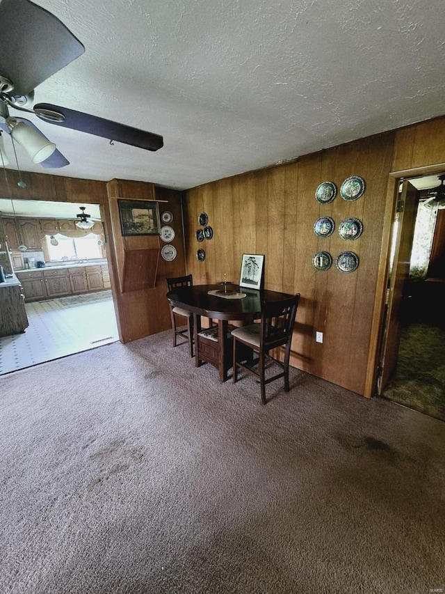 dining room featuring ceiling fan, carpet, wood walls, and a textured ceiling