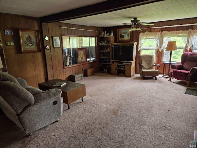 carpeted living room featuring wood walls, beamed ceiling, and ceiling fan