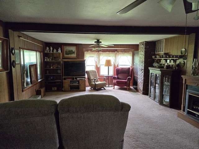 living room with ceiling fan, a textured ceiling, a large fireplace, brick wall, and carpet floors