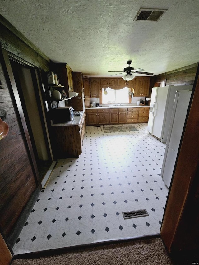 kitchen with wooden walls, white fridge, tile floors, and ceiling fan